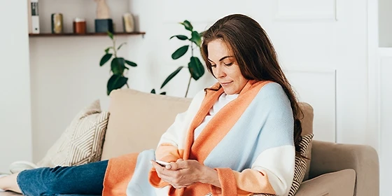  Junge Frau mit iPhone liegt auf Sofa.
